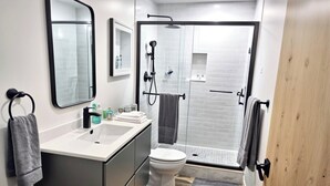 A modern bathroom with a sink, mirror, toilet, and shower area.