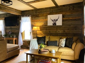 A cozy living room with a wooden wall, a sofa, a coffee table, and a TV mounted on the wall. - The Forge Cabin, A Charming and Spacious renovated cabin.  Everyone loves it! (Livermore)