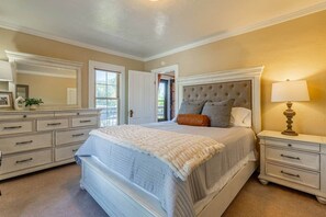 A bedroom with a large bed, a dresser, a nightstand, and a lamp.