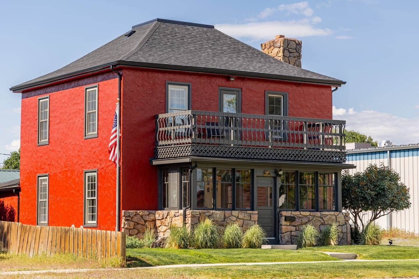 A two-story red house with a stone facade, a balcony, and a flag.