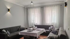 A living room with a sofa set, a dining table, and a chandelier.