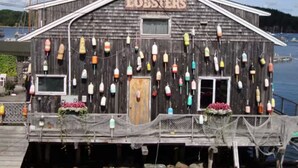 Un bâtiment en bois sur lequel est affiché un panneau indiquant « HOMARDS », et diverses bouées colorées sont suspendues à l’extérieur.
