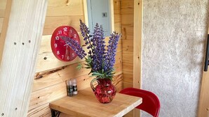 L’intérieur d’un chalet en bois, avec une table en bois, deux chaises rouges, une horloge rouge, un vase avec des fleurs violettes et une porte.