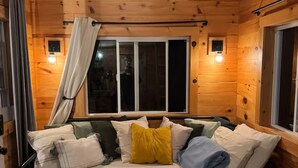 Une pièce de cabane en bois comprenant un lit, une fenêtre et un luminaire au plafond.