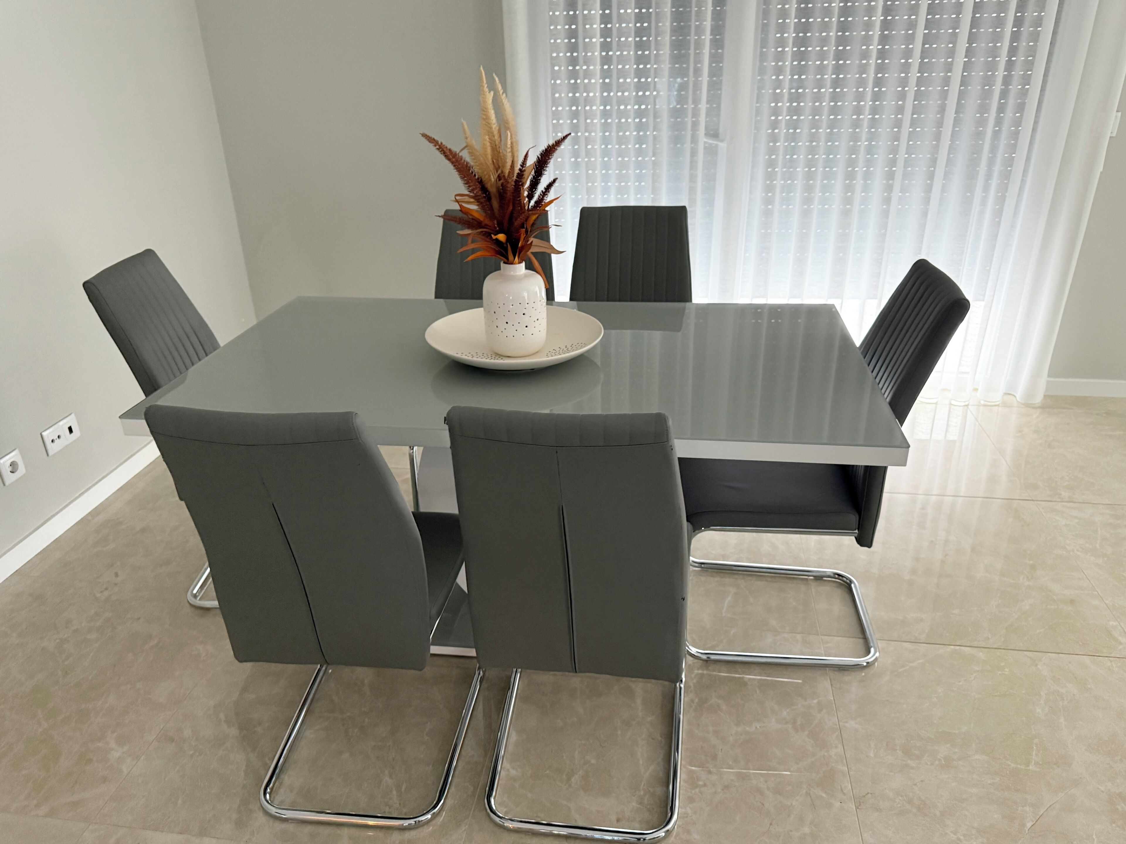 A modern dining table with four chairs, a decorative vase, and a plate on the table.