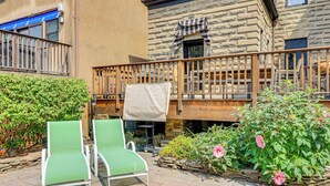 Un patio con dos sillones verdes, un muro de piedra y una barandilla de madera en el balcón.