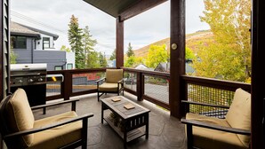 Un patio al aire libre con una parrilla, asientos y vistas a árboles y colinas.