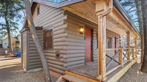 Eine Blockhütte mit einer Holzterrasse, einer roten Tür und einem kleinen angebauten Schuppen.