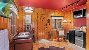 Ein Blockhaus-Interieur mit Holzausstattung, einer Küchenzeile, einem Esstisch mit Stühlen, einer Couch und Blick auf eine Berglandschaft.