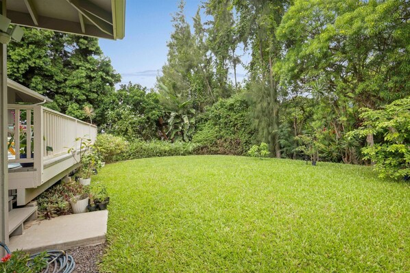 Un patio trasero bien cuidado con césped, una terraza de madera y diversas macetas con plantas.
