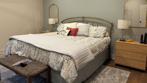 Une chambre à coucher comprenant un lit, des tables de chevet, un banc et une commode.