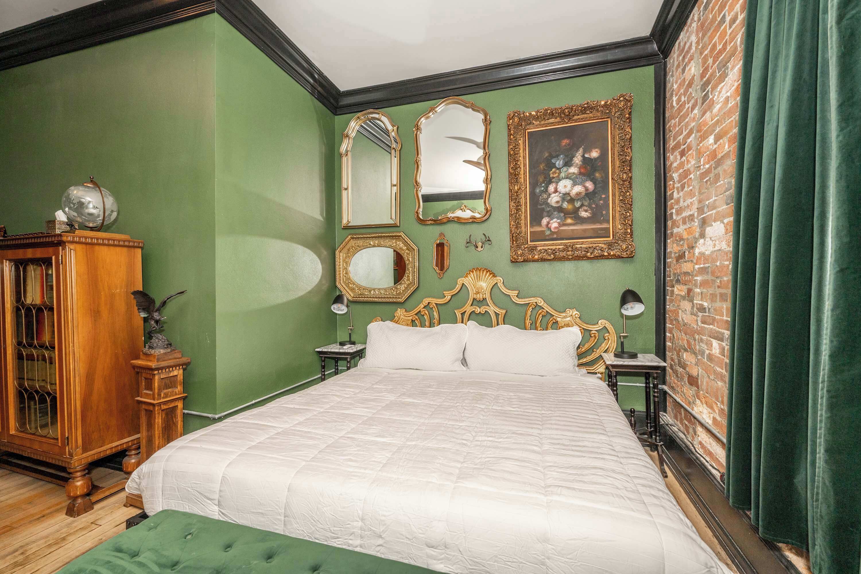 A room with a large bed, green walls, a wooden cabinet, and a brick wall.