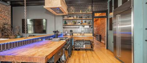 A modern kitchen with a wooden countertop, stainless steel appliances, and a brick wall.