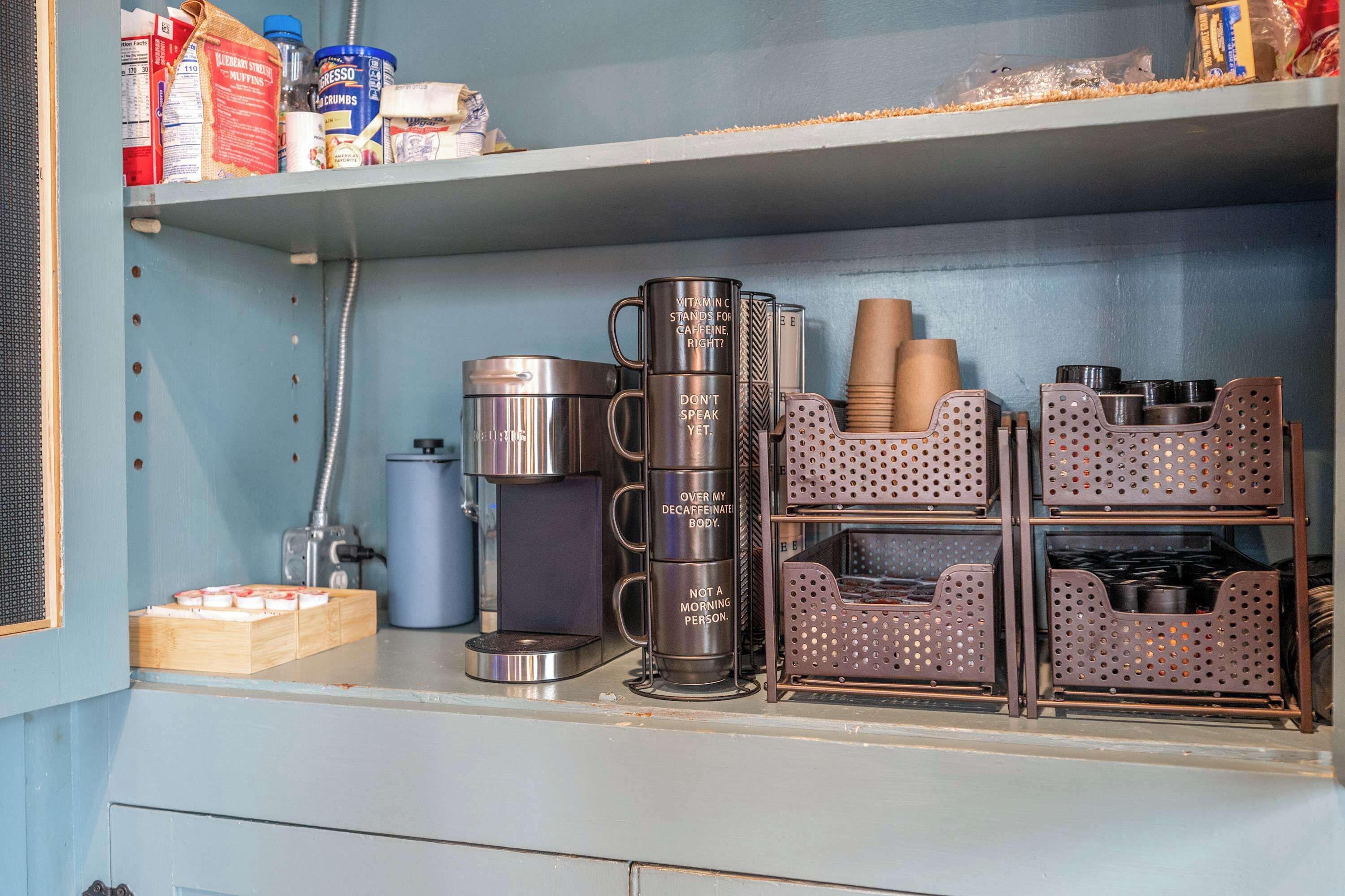 Un comptoir de cuisine sur lequel on trouve divers objets, notamment une machine à café, un thermos et des récipients de rangement.