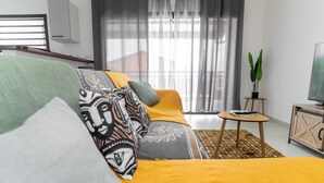 A modern bedroom with a sofa bed, a small table, a potted plant, and a TV on a cabinet. - Le Nid de Thalys  Appartement de charme (Cayenne)