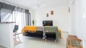 A modern living room with a sofa, a TV, a small table, and a chair. - Le Nid de Thalys  Appartement de charme (Cayenne)