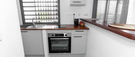 Een compacte keuken met een inbouwoven, een spoelbak en een raam met zonwering.