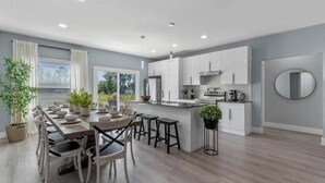A modern kitchen with white cabinets, a central island, and a dining area with a long table and chairs.