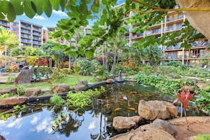 Un patio de hotel con un estanque, abundante vegetación y varios balcones.