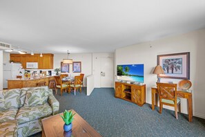 A compact living space with a kitchenette, a dining area, a sofa, a TV, and a desk with a lamp.
