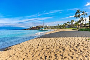 A beach with a sailboat, palm trees, and a hotel in the background.