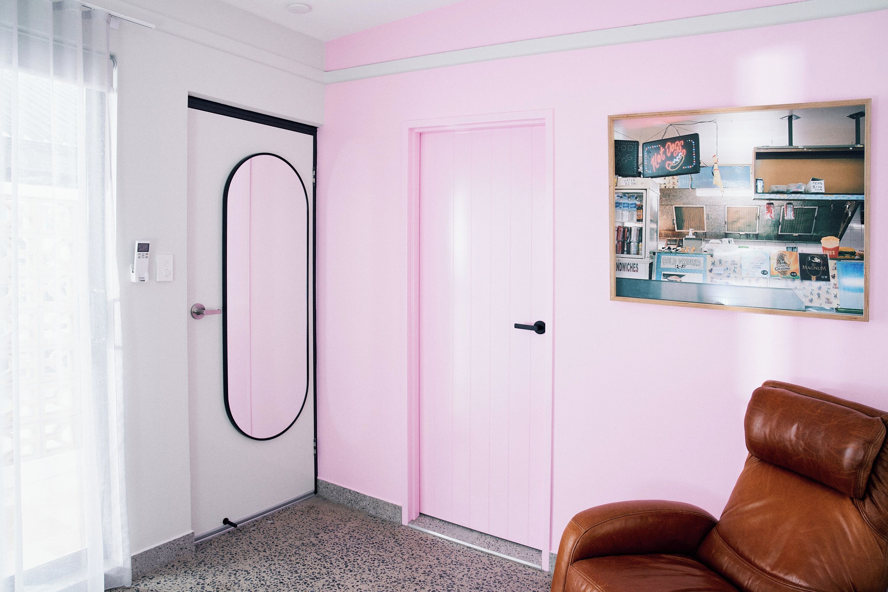 A room with a pink door, a brown leather chair, a framed picture on the wall, and a window with sheer curtains.