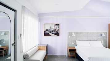 A modern hotel room with a bed, a bench, a small table, and a picture on the wall.
