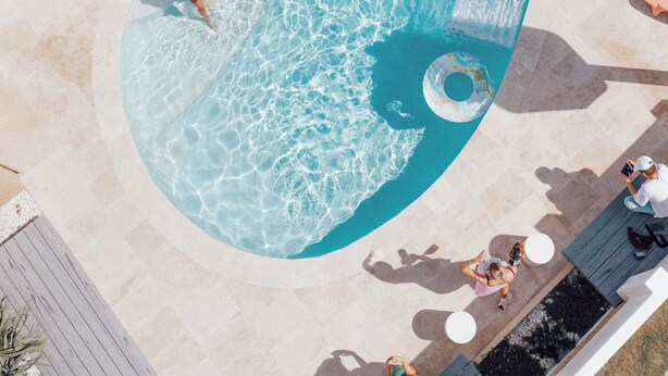 An aerial view of a swimming pool with clear water, surrounded by lounge chairs and a wooden deck.