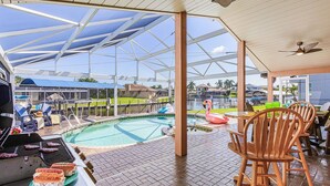 An outdoor pool area with a grill, lounge chairs, and a flamingo float. - Sail into Paradise with Pool, Spa & Dockside Living - Captain Jack's Landing (Cape Coral)