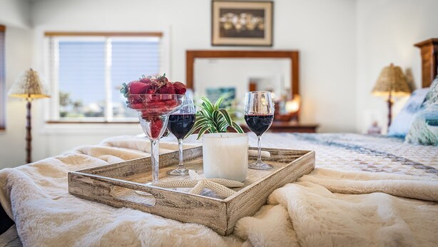 A cozy bedroom with a wooden tray holding glasses of wine, a candle, and a bowl of fruit. - Sail into Paradise with Pool, Spa & Dockside Living - Captain Jack's Landing (Cape Coral)