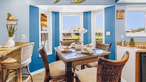 A dining area with a table set for four, surrounded by wicker chairs, a decorative fish wall hanging, and a view through a window. - Sail into Paradise with Pool, Spa & Dockside Living - Captain Jack's Landing (Cape Coral)