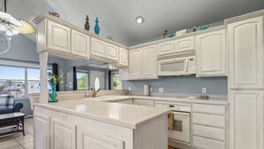 A kitchen with white cabinetry, a central island, a microwave, and a dishwasher. - Driftwood Den - Resort Pools, Golf, Sleeps 6 (Port Isabel)