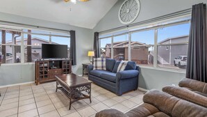 A living room with a TV, sofa, and a clock on the wall. - Driftwood Den - Resort Pools, Golf, Sleeps 6 (Port Isabel)