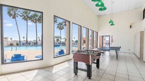 A room with large windows, a foosball table, and a pool view. - Driftwood Den - Resort Pools, Golf, Sleeps 6 (Port Isabel)