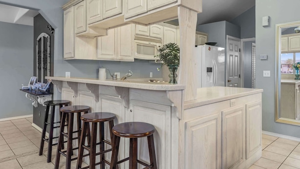 A kitchen with a bar area, white cabinetry, and three stools. - Driftwood Den - Resort Pools, Golf, Sleeps 6 (Port Isabel)