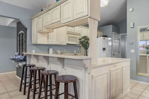 A kitchen with a bar area, white cabinetry, and three stools. - Driftwood Den - Resort Pools, Golf, Sleeps 6 (Port Isabel)