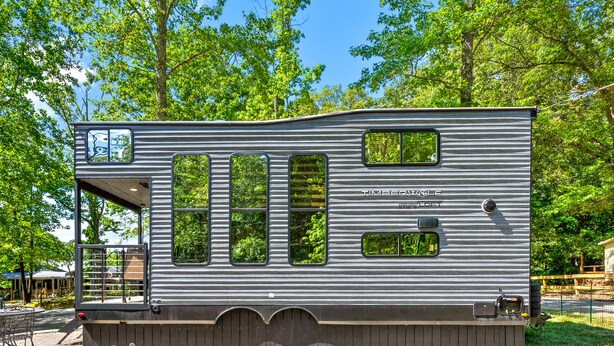 Une maison mobile dotée de nombreuses fenêtres, d’un porche couvert et d’une allée en gravier.