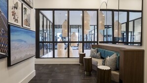 A modern interior with large windows, a seating area with a sofa and round tables, and artwork on the walls.