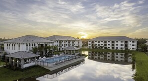 A modern hotel with a pool, reflecting buildings, and a sunset.