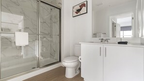 A modern bathroom with a glass-enclosed shower, a white toilet, and a white vanity with a mirror.