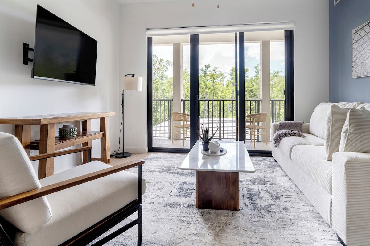 A modern living room with a flat-screen TV, a wooden coffee table, a sofa, and a balcony with chairs.