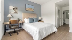 A bedroom with a large bed, two nightstands, a chair, and a headboard. There are two wall-mounted lamps and a framed picture above the bed.