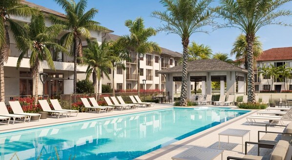 A swimming pool with lounge chairs, palm trees, and a building with balconies.