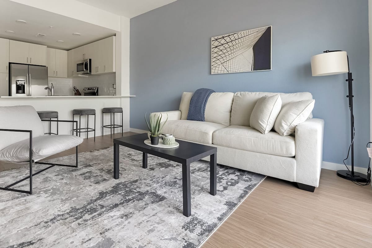 A modern living room with a sofa, armchair, coffee table, and a kitchen in the background.