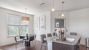 A modern kitchen with a granite countertop, a sink, and a dining area with chairs and a table. - Landing Bradenton Near G.T. Bray Park (Bradenton)