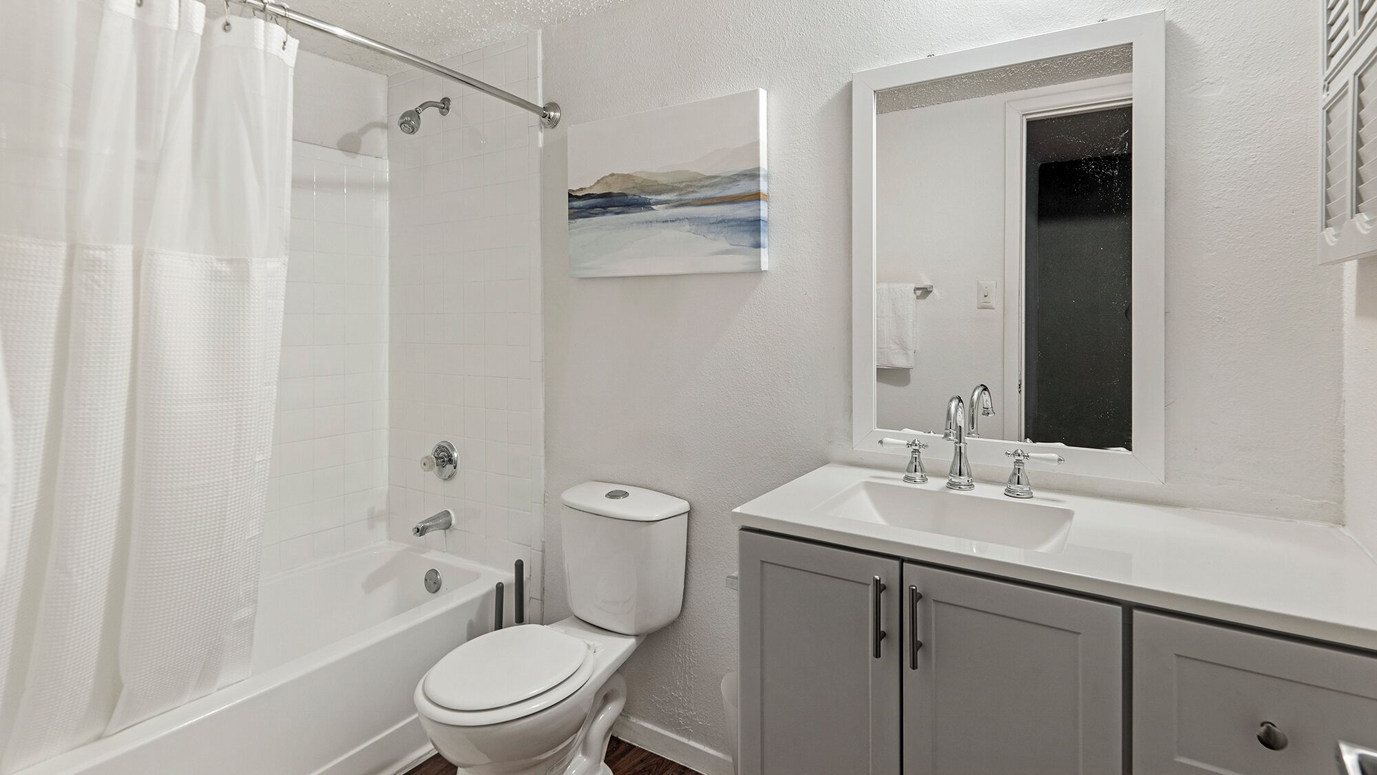 A bathroom with a shower, toilet, sink, and a painting on the wall.