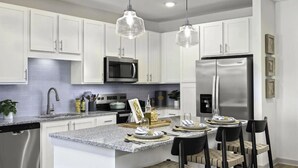 Una cocina moderna con armarios blancos, un refrigerador de acero inoxidable, un microondas y lámparas colgantes.