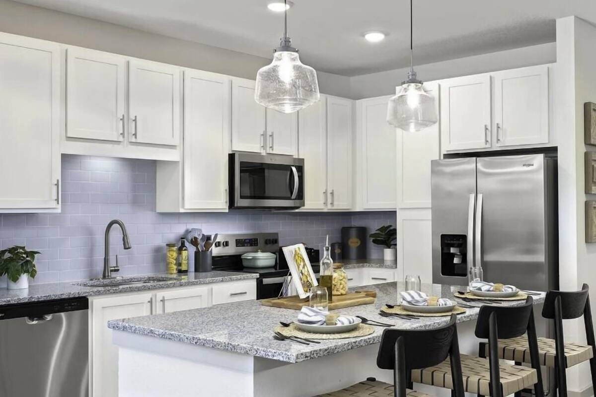 A modern kitchen with white cabinets, a stainless steel refrigerator, a microwave, and pendant lights.