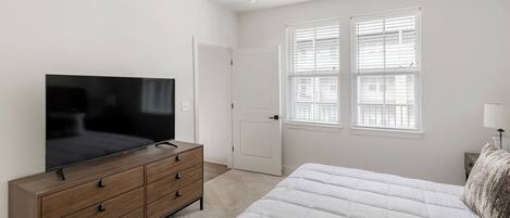 Un dormitorio con una cama, un aparador de madera con televisor, una puerta y ventanas con persianas.