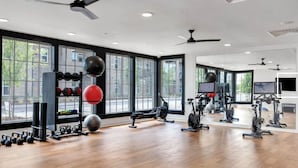 A modern gym with exercise equipment, large windows, and a wooden floor. - Landing Apartments At Town Madison (Madison)